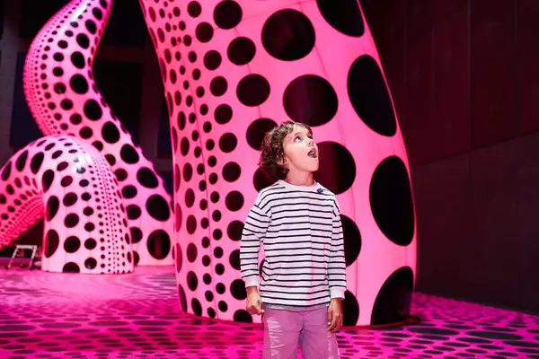 A child stands in a Yayoi Kusama exhibition with pink and black tentacles