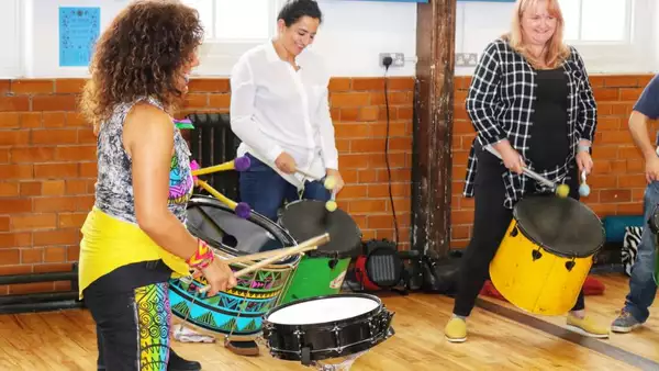 Photo of three people drumming in a circle