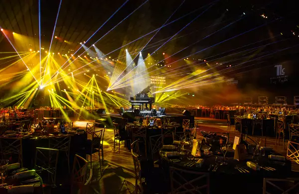 Large circle tables set up in the Warehouse for the Great Mancunian Ball. There are yellow laser lights and a grand piano in the centre.