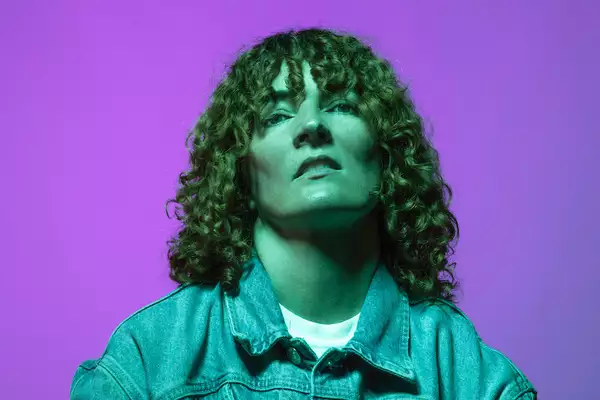 Electronic artist Planningtorock stands against a purple background wearing a denim jacket
