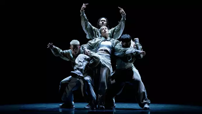 A group of five performers dancing on stage during CYCLES, dressed in loose-fitting, modern streetwear, against a dark background.