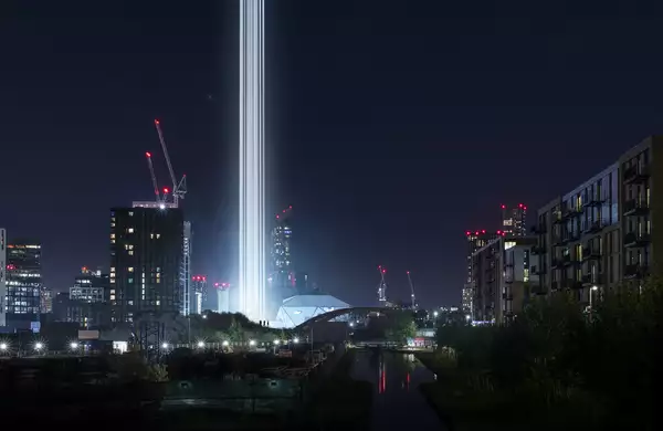 A Manchester cityscape at nighttime with bright columns of light visible next to the Factory International building.