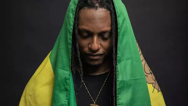 Artist J Chambers looking down draped in a flag thats green and yellow
