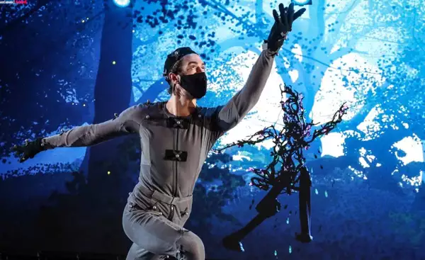 Man in grey costume performing in front of a screen projection