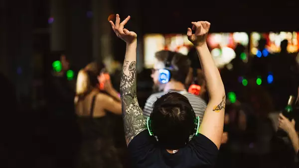 Photo of a person with their back turned, dancing with headphones in a crowd