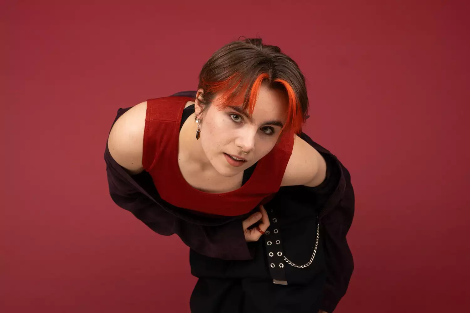 Tallulah Guard wearing black and red clothing, on a red background. They are looking up at the camera.