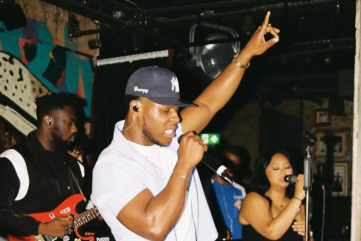 Grumpy performing on stage, singing into a microphone with eyes closed and a hand in the air. Behind them, two people sing and play guitar.