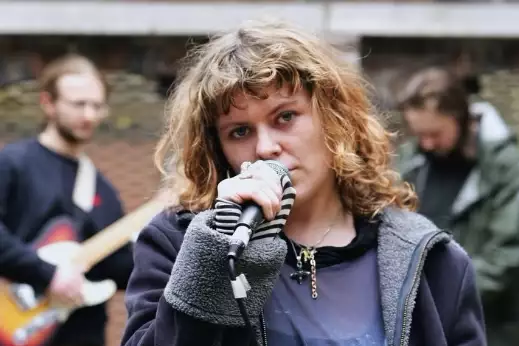 Shell Company performing outside. There is a singer in focus, and two other performers blurred out behind them.