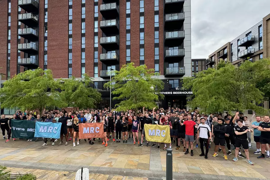 A large group of people wearing running gear outside, holding signs that say MRC