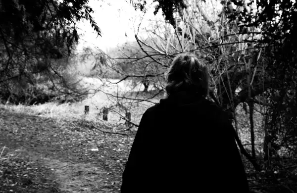 black and white photo of a woman walking through a forest
