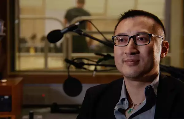 Huang Ruo smiling inside a recording studio with microphones behind him