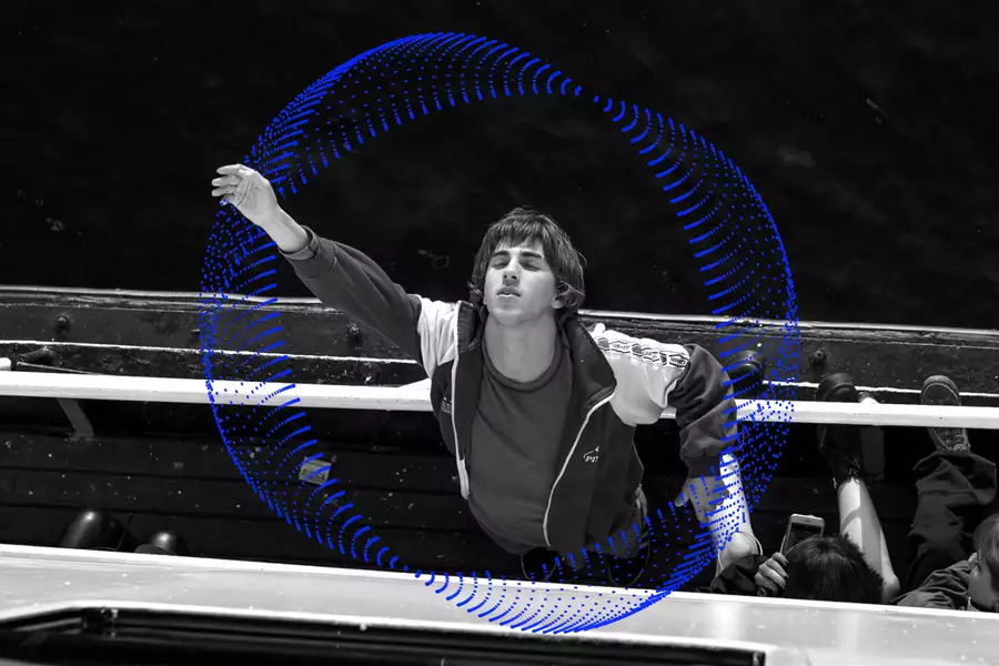 A still from the film Crossing. A male character wearing a tracksuit jacket is leaning off the edge of a boat and reaching up to the sky with his eyes closed.